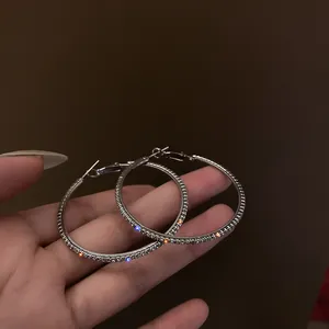 Dettaglio di orecchini a cerchio in argento scintillanti con cristalli in mano.