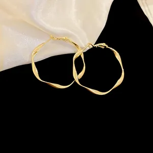 Macro view of elegant golden twisted hoop earrings displayed on white satin fabric