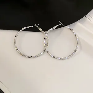 Detailed close-up of large silver-toned twisted hoop earrings on a neutral background.