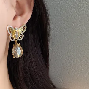 Close-up of gold hollow butterfly earrings with champagne teardrop crystal dangle.
