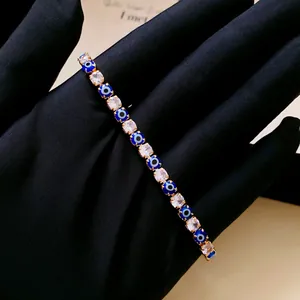 Close-up of elegant gold evil eye tennis bracelet with clear zircons on black glove.