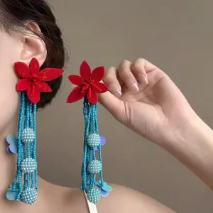 Detailed view of red flower earrings with long blue beaded tassels on model