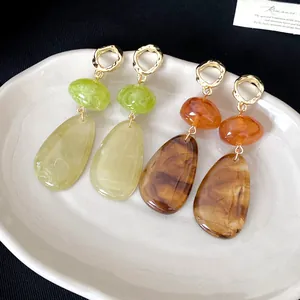Close-up of retro teardrop earrings featuring marbled resin in green and amber tones