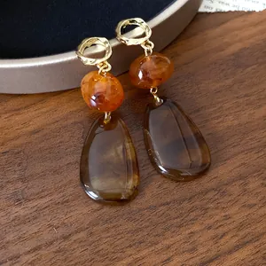 Close-up of retro drop earrings with amber resin beads and golden hammered hoops.