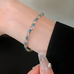 Close-up of gold-tone bracelet with white cubic zirconia and blue evil eye beads on wrist
