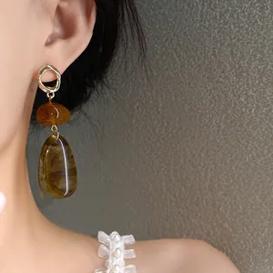 Detailed close-up showing vintage amber-colored water drop earrings on model's ear with pearl strap
