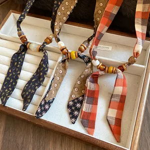 Three bohemian necklaces with fabric ribbons, wooden beads, and ceramic accents in a display box.