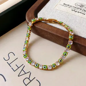 Close-up of gold-plated bracelet with green evil eye and round zircon stones