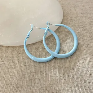 Dettaglio ravvicinato di eleganti orecchini a cerchio in smalto azzurro su sfondo strutturato