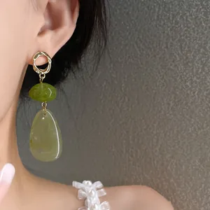 Close-up of vintage teardrop earrings featuring green resin beads and gold rings.