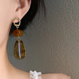 Close-up of vintage amber-colored waterdrop earrings with hammered gold studs.