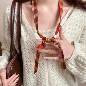 Close-up detail of Bohemian style fabric necklace with orange plaid and colorful wood beads