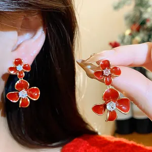 Close-up detail of vibrant red enamel flower earrings with sparkling central zircon on model