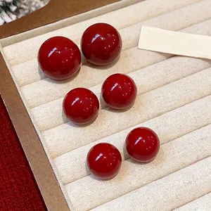 Elegante tiefrote Perlenohrstecker mit Silbernadeln in einer beigen Schmuckschale präsentiert
