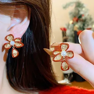 Detailed close-up showing the elegant red flower stud earrings with gold texture and pearl