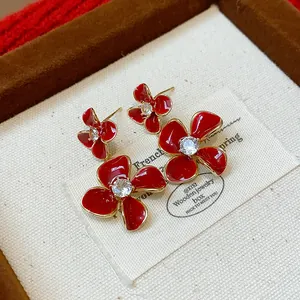 Close-up macro detail of red enamel flower earrings with central zircon in a jewelry box.