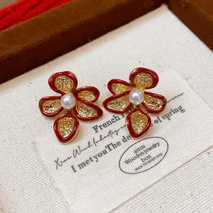 Detailed macro view of red enamel flower stud earrings with central pearl and gold plating