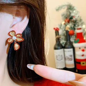 Close-up view of an elegant red enamel flower stud earring with central pearl worn on ear