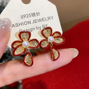 Macro view of detailed 18k gold plated flower earrings featuring red petals and pearls