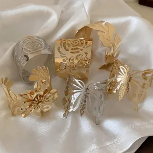 Close-up detail of elegant gold and silver floral metal open cuff bracelets on white silk.