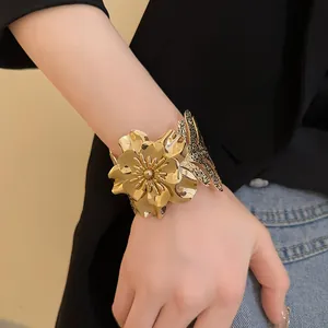Detailed shot of a large gold flower open cuff bracelet worn on a wrist over a black jacket.