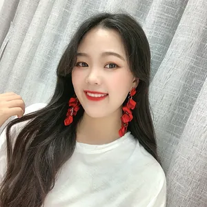 Vue détaillée de longues boucles d'oreilles à pompons en pétales de tissu rouge sur un modèle