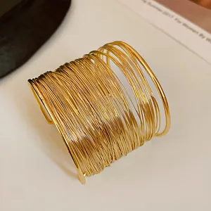 Detailed macro shot of a gold multi-strand wire wrap wide cuff bracelet on a white surface.