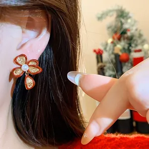 Close-up of a red 18k gold plated flower stud earring with pearl worn on an ear