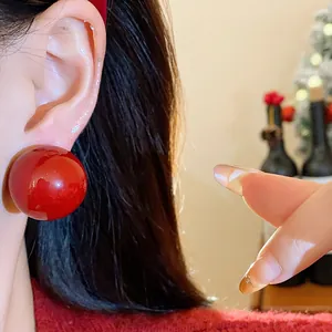 Detailansicht eines glänzend roten Kugelohrsteckers am Ohr für einen festlichen Look.