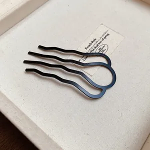 Macro detail of a minimalist matte black wave-shaped U-hair fork on a prop card.