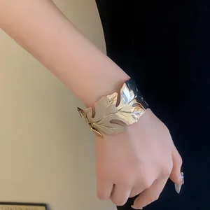 Detailed close-up showing the metallic texture of a gold leaf-shaped open cuff bracelet