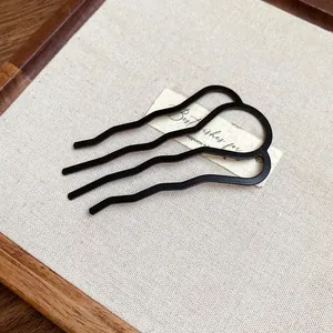 Close-up of minimalist black wave-shaped U hair fork for bun styling.
