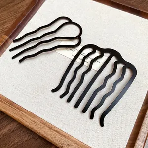 Close-up of minimalist black wave U-shaped hair forks displayed on a rustic wooden tray.
