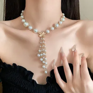 Detailansicht einer eleganten Perlen-Quastenhalskette mit Goldblume, getragen von einem Model.