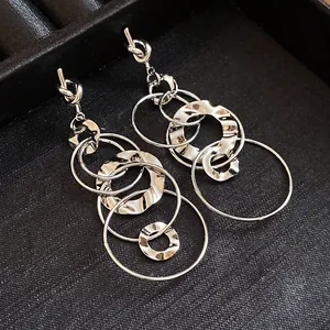 Close-up detail of silver knotted tassel earrings featuring interlocking pleated hollow circles.