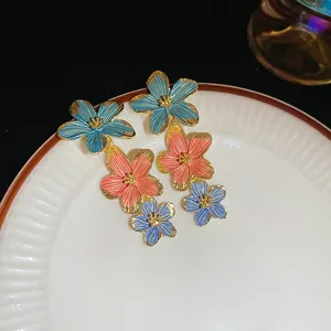 Close-up of layered floral earrings with blue and pink enamel petals on a ceramic plate