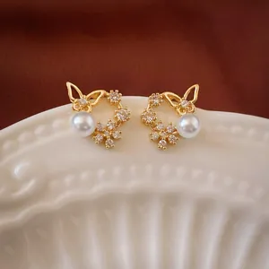 Close-up detail of gold butterfly stud earrings with white pearls and zirconia stones