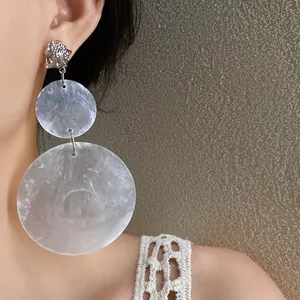 Detalle de primer plano de pendientes colgantes redondos plisados de plata en una modelo