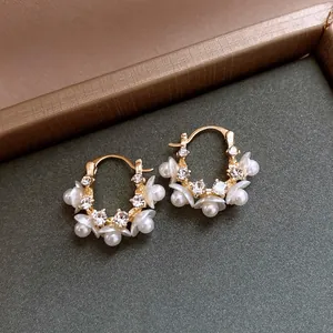 Close-up detail of elegant gold hoop earrings with white floral pearls and crystals