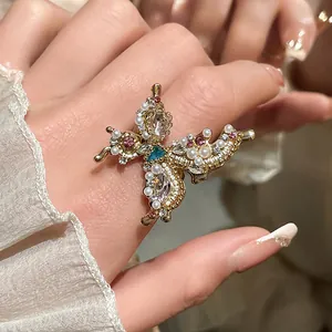 Detailed view of an ornate gold butterfly ring with pearls and rhinestones on finger