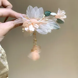 Delicate pink fabric flower hair clip with pearl tassels and leaves on a hand-held shot