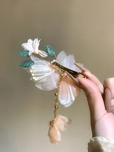 Detailed view of an elegant fabric flower hair clip with a long golden tassel and leaves