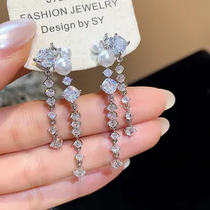 Close-up detail of elegant long dangle earrings featuring white pearls and sparkling cubic zirconia
