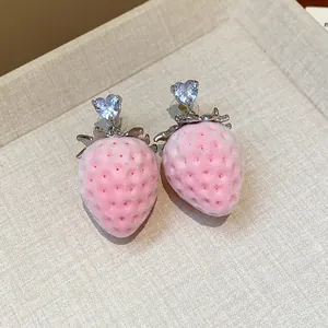 Primo piano di orecchini a forma di fragola rosa floccata con cristalli a cuore scintillanti.