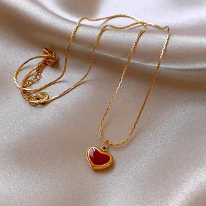 Close-up of elegant gold chain necklace with a vibrant red enamel heart pendant.
