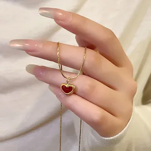 Detail showing an elegant gold necklace with a red heart pendant held by hand.
