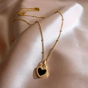Detail shot of an elegant gold necklace with a black oil-drip heart pendant on silk