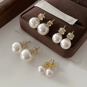 Four pairs of high-luster round pearl stud earrings with gold posts on jewelry box.