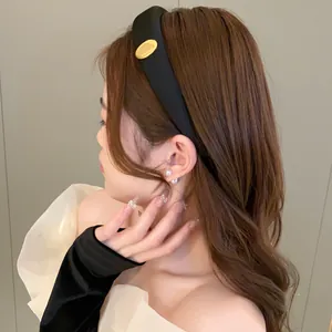 Close-up view of a stylish black sponge headband with a gold oval detail on a model