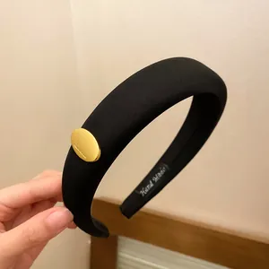 Close-up detail of a thick black sponge headband with a gold oval decorative accent